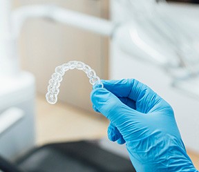 Dentist with blue glove holding clear aligner