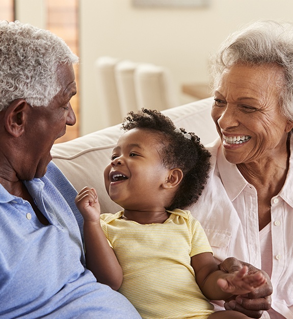 Grandparents smiling with grandchild after dental implant tooth replacement