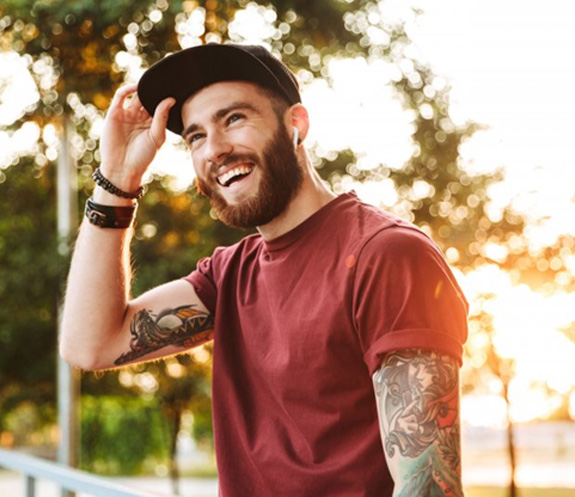 Man with a hat and tattoos smiling outdoors