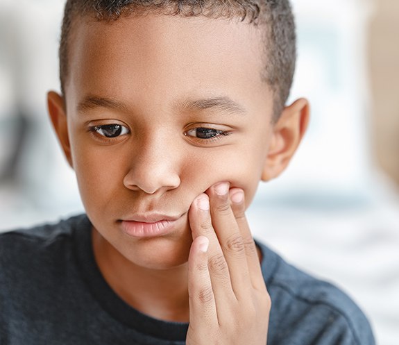 Child in need of emergency dentistry holding cheek