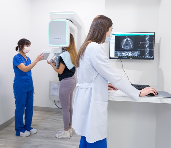 Patient receiving 3 D cone beam imaging scans as dentist reviews them