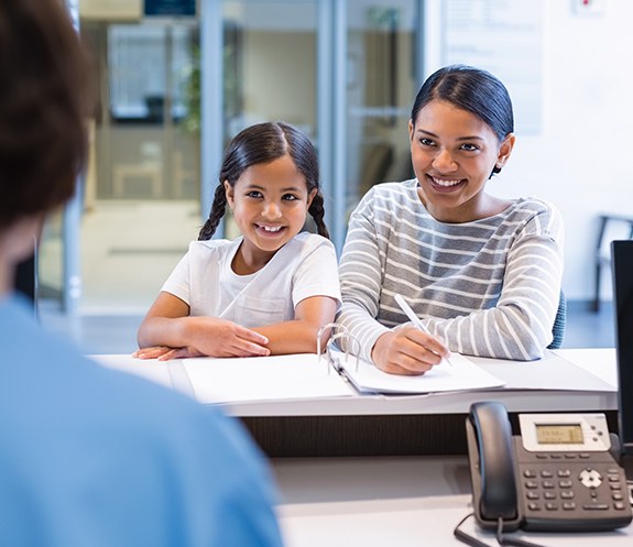 Mother and daughter completing dental insurance forms at reception desk