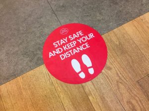 red sign on floor that reads “stay safe and keep your distance” 