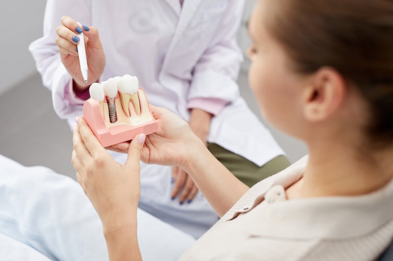 A dentist showing a dental implant model to their female patient