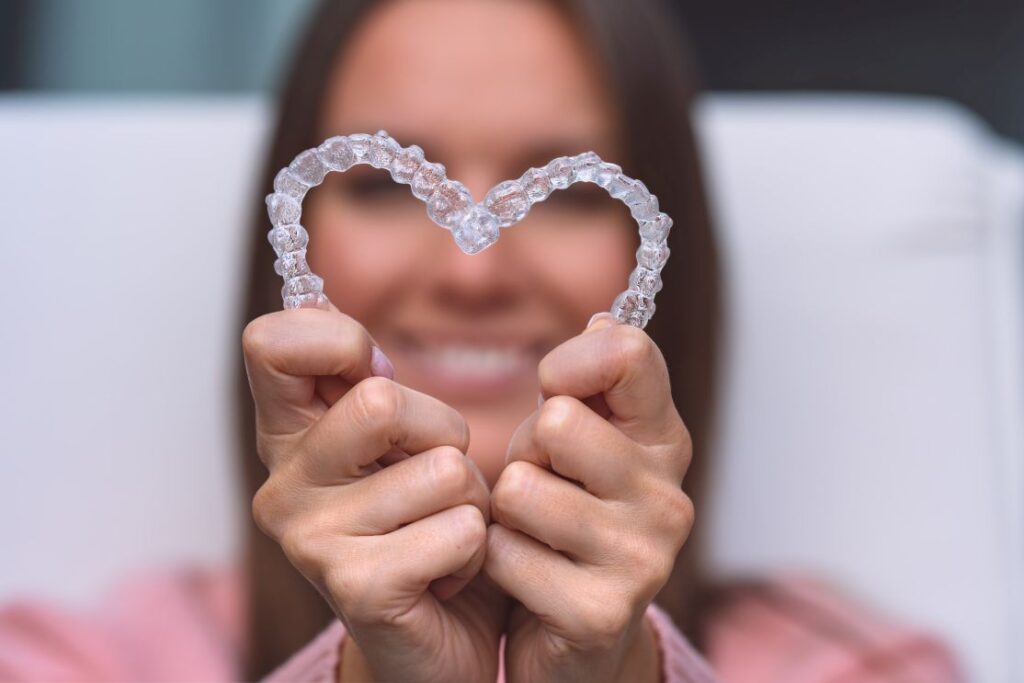 A woman making a heart with Invisalign aligners